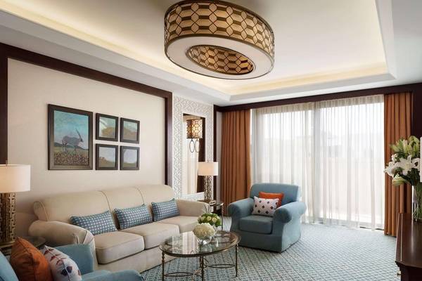 Wohnzimmer des Al Najada Doha Hotel by Tivoli mit Sofa, Stühlen, Tisch, Lampen und Bildern an der Wand.