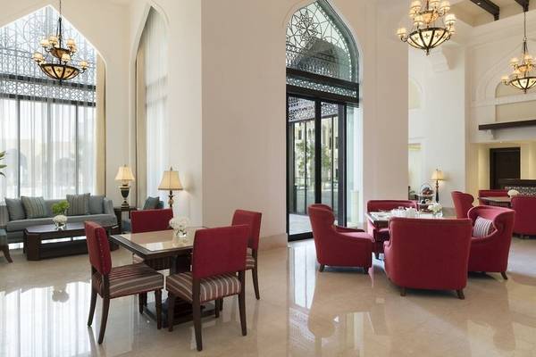 Lobby des Al Najada Doha Hotel by Tivoli mit roten Stühlen, Tisch, Kronleuchtern und Sofas.