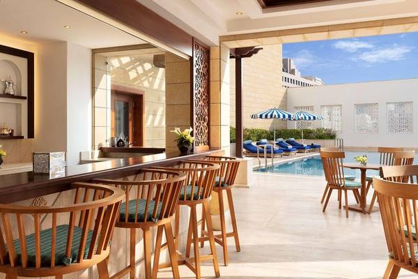 Innenansicht der Poolbar des Al Najada Doha Hotel by Tivoli mit hölzernen Stühlen und Tischen.
