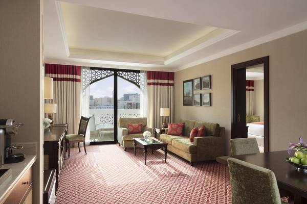 Innenansicht der Suite im Al Najada Doha Hotel by Tivoli mit Wohnzimmer, Esstisch und Blick auf die Stadt.