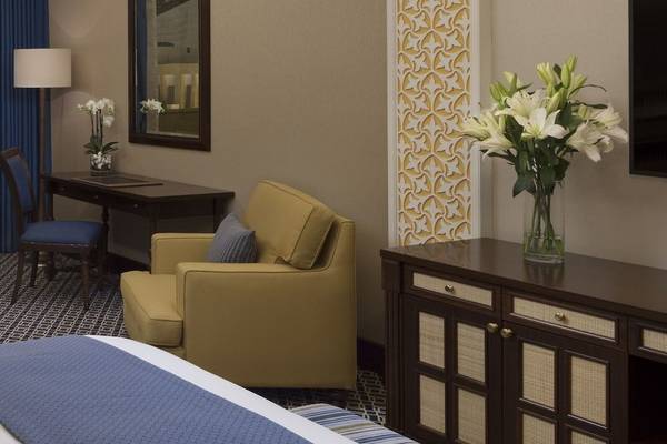 Innenansicht eines Zimmers im Al Najada Doha Hotel mit einem Bett, einem Schreibtisch, einem Stuhl und einem Fernseher.