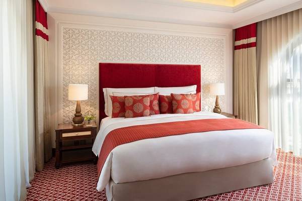 Schlafzimmer im Al Najada Doha Hotel by Tivoli mit rotem Kopfteil, weißen und roten Kissen und zwei Lampen auf Nachttischen.