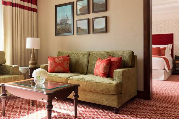 Suite-Wohnzimmer im Al Najada Doha Hotel by Tivoli mit grünem Sofa, rotem Kissen und kunstvollen Gemälden an der Wand.