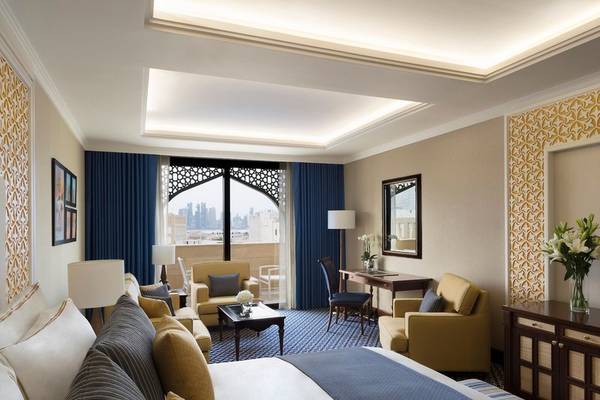 Innenansicht eines Zimmers im Al Najada Doha Hotel by Tivoli mit großem Bett, Wohnzimmermöbeln und Stadtblick.