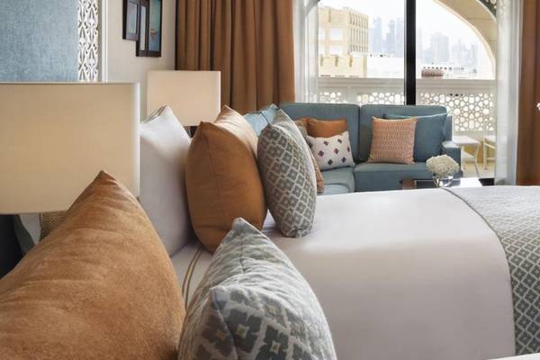 Innenansicht eines Zimmers im Al Najada Doha Hotel by Tivoli mit Bett, Sofa und Fenstern.
