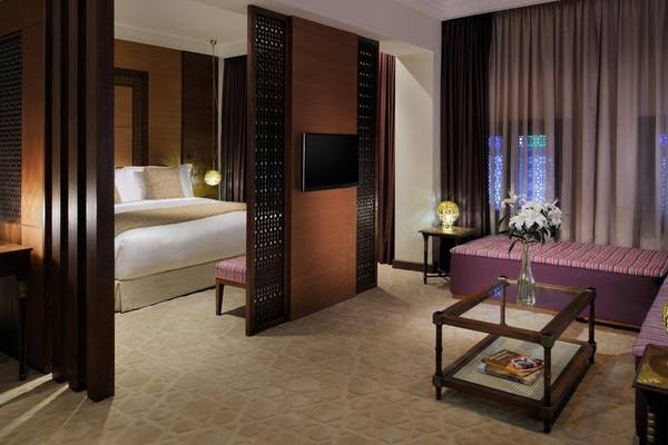 Schlafzimmer im Souq Waqif Boutique Hotels mit Doppelbett, Fernseher, Tisch, Sofa und Blumenvase.