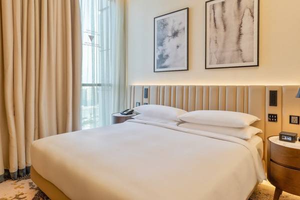 Schlafzimmer im Embassy Suites By Hilton Doha Old Town mit einem großen Bett, weißen Kissen und zwei kunstvollen Bildern an der Wand.