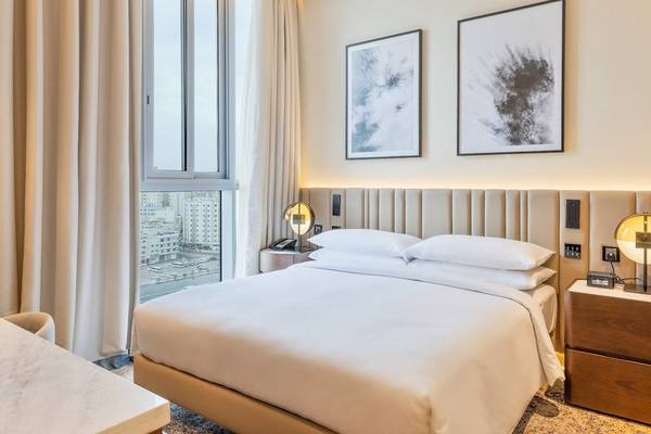 Innenansicht eines Schlafzimmers im Embassy Suites By Hilton Doha Old Town mit großem Bett, weißen Kissen und zwei Bildern an der Wand.