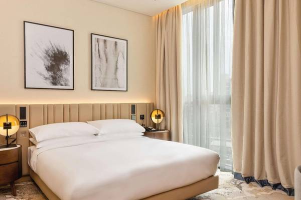 Schlafzimmer im Embassy Suites By Hilton Doha Old Town mit Doppelbett, Nachttischen und Gemälden an der Wand.