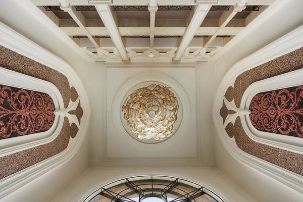 Innenansicht des Marsa Malaz Kempinski, The Pearl mit goldenem Kronleuchter und rotem Wandmuster.