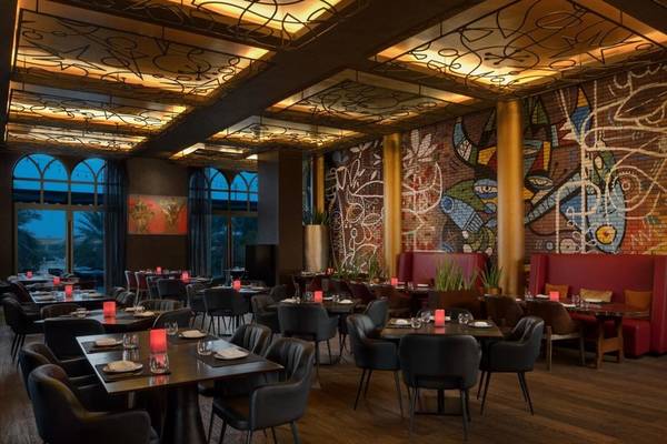 Innenbereich des Marsa Malaz Kempinski, The Pearl Restaurants mit geometrischen Wandgemälden und gedeckten Tischen.