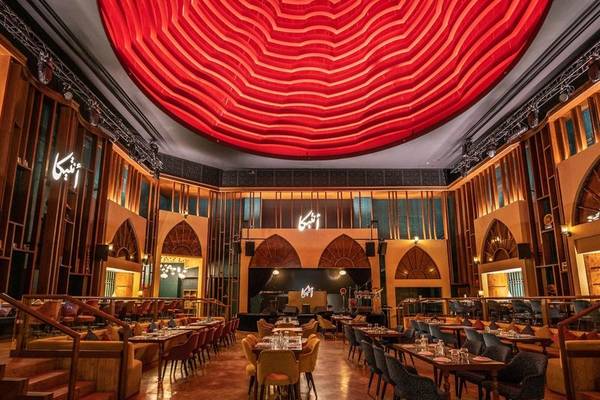 Innenbereich des Marsa Malaz Kempinski, The Pearl mit rotem Deckendesign und vielen Tischen und Stühlen.
