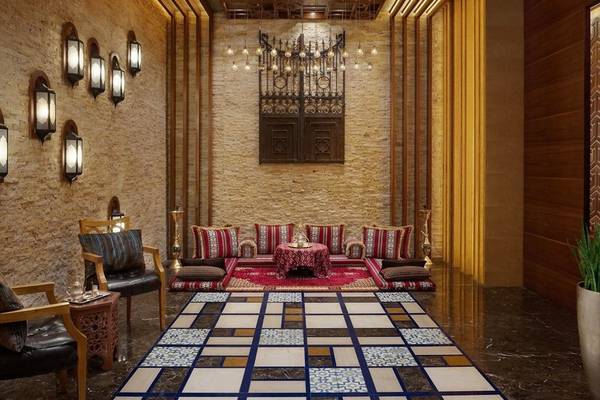 Innenbereich des Marsa Malaz Kempinski Hotels mit brauner Wand, Fliesenboden, Sofas, Tisch und Wandleuchten.