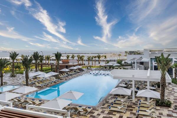 Aussicht auf den Poolbereich des Rixos Gulf Hotel Doha mit Loungeliegen und Sonnenschirmen