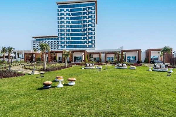 Außenbereich des Rixos Gulf Hotel Doha mit Rasen, Möbeln und hohen Gebäuden