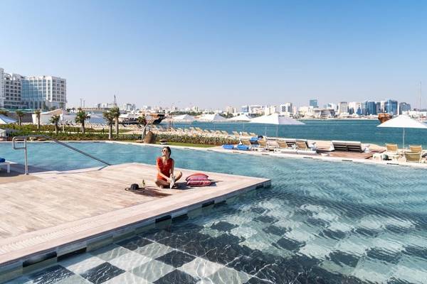 Ein Gast sitzt am Rand des Pools im Rixos Gulf Hotel Doha mit Blick auf die Stadt.