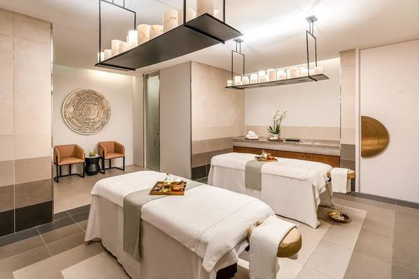 Behandlungsraum im Spa des Rixos Gulf Hotel Doha mit zwei Massagetischen, Sesseln und einem Wandbild.