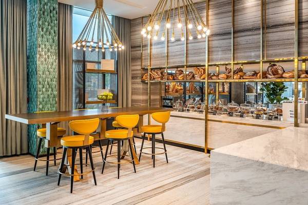 Innenraum des Rixos Gulf Hotel Doha mit gelben Stühlen und einem Esstisch vor einer goldenen Wand mit Bäckereiprodukten.