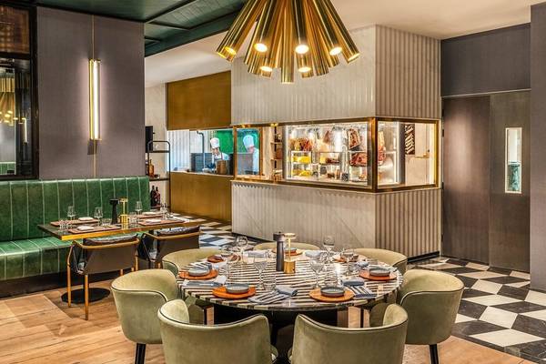 Innenbereich des Rixos Gulf Hotel Doha mit modernem Restaurant, grünen Sesseln und zentralem Tisch.