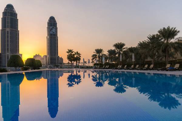 Sonnenuntergang über dem Pool des Grand Hyatt Doha Hotel & Villas mit reflektierten Gebäuden und Palmen.