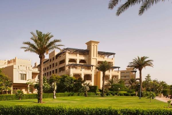 Außenansicht des Grand Hyatt Doha Hotel & Villas mit mehreren Gebäuden, Palmen und Rasenflächen.