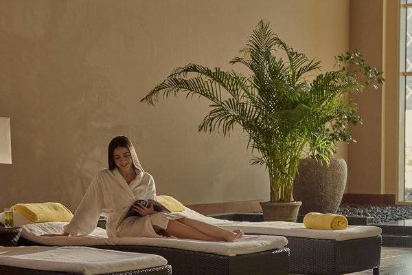 Frau im Bademantel liest auf einer Liege im Spa-Bereich des Grand Hyatt Doha Hotel & Villas.