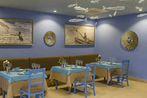 Innenansicht des Restaurants im Royal Taj Mahal Hotel mit blauen Tischen und Stühlen, Fischbildern an der Wand und einer langen Bank.