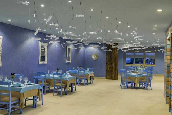 Innenansicht des Restaurants im Royal Taj Mahal Hotel mit blauen Tischen, Stühlen und dekorativen Fischfiguren an der Decke.