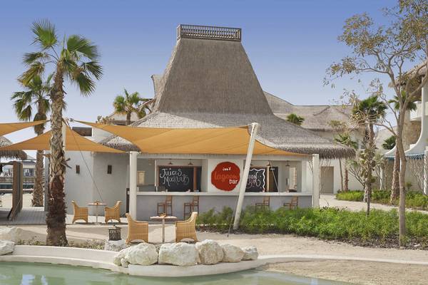 Außenansicht der Pool-Bar im Banana Island Resort Doha von Anantara mit Palmen und einem Pool davor.