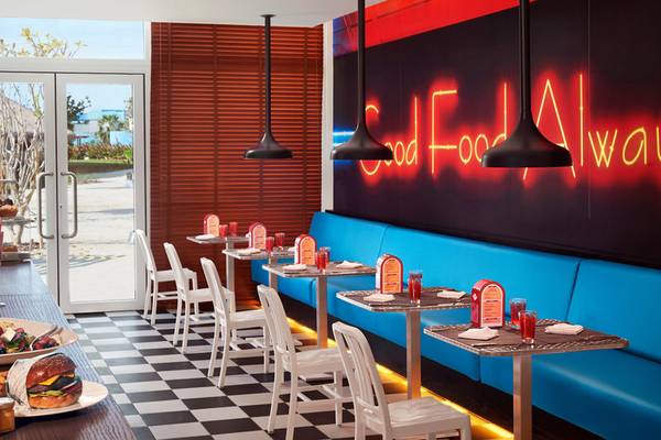 Interieur von Banana Island Resort Doha by Anantara mit Esstischen, neon Schriftzug 'Good Food Always' und roten Neonbeleuchtung.