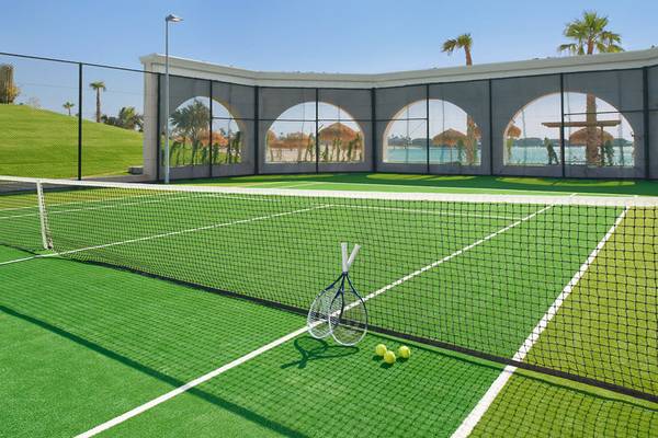 Tennisplatz im Banana Island Resort Doha von Anantara mit Schlägern und Tennisbällen auf dem grünen Platz.