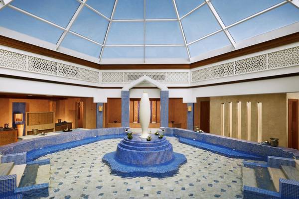 Innenansicht des Pools im Banana Island Resort Doha von Anantara mit Glasdach, blauen Fliesen und zentraler Vase.