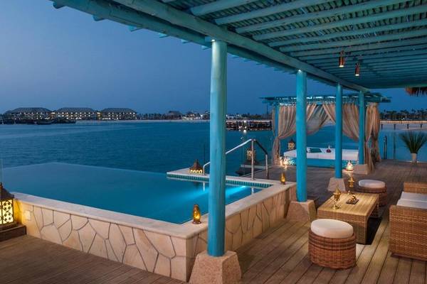 Poolbereich des Banana Island Resort Doha von Anantara bei Nacht mit Überdachung, Sitzmöbeln und Blick aufs Meer.