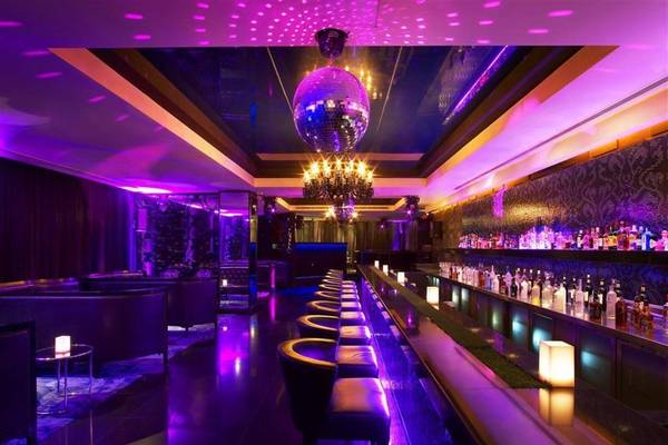 W Doha Hotel & Residences Bar Innenraum mit lila Beleuchtung, glänzenden Stühlen und einer gut bestückten Bar.