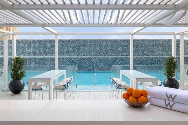 Pool im W Doha Hotel & Residences mit blauen Stühlen und Wasserfall.