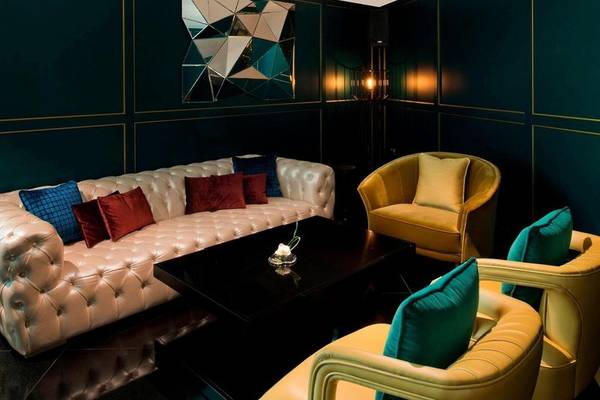 Loungebereich im W Doha Hotel & Residences mit dunkelgrünen Wänden, weißen Möbeln und gepolsterten Sesseln.