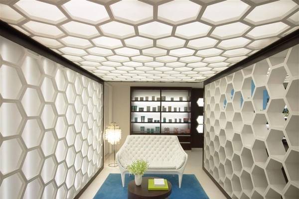 Inneneinrichtung des W Doha Hotel & Residences mit weißen Hexagon-Wänden, einem weißen Sofa, einem runden Tisch und einer Lampe.