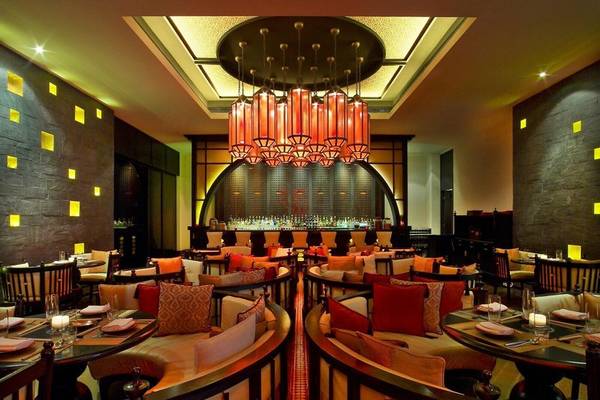 Innenraum des W Doha Hotel & Residences mit Tisch, Stühlen, Kissen und roten Laternen.