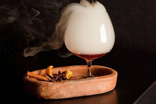 Cocktail mit Raucheffekt im Glas, serviert auf einem Tablett mit Gewürzen.