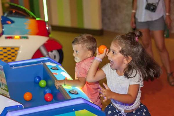 Zwei Kinder spielen in einer Spielhalle mit bunten Bällen und einem Motorrad im Hintergrund.