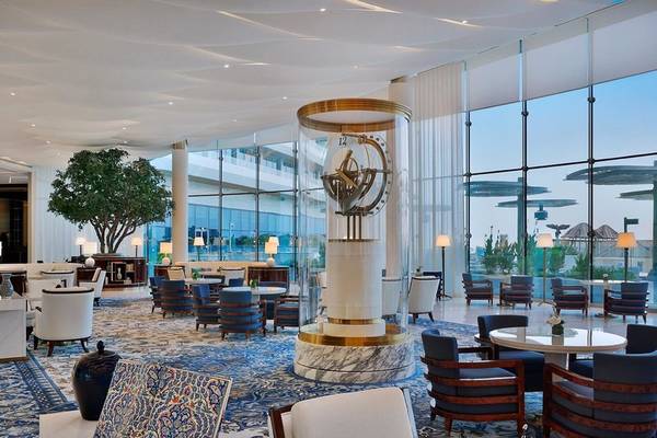 Innenbereich des Waldorf Astoria Doha Lusail Hotel mit modernen Möbeln, großen Fenstern und einer zentralen Uhr.