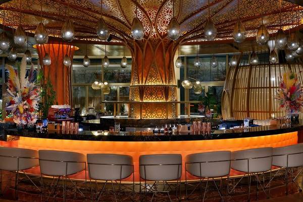 Bar im Waldorf Astoria Doha Lusail Hotel mit orangefarbenen Stühlen und einer großen Baumskulptur.