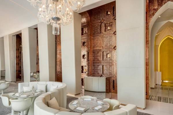Innenansicht des Fairmont Doha Restaurants mit weißen Möbeln, braunen Wänden und einem großen Kronleuchter.