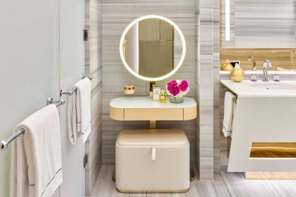 Badezimmer im Fairmont Doha Hotel mit weißem Waschtisch, Spiegel und goldenem Hocker.