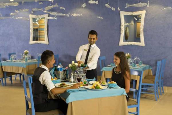 Ein Kellner serviert ein Paar im Royal Taj Mahal Hotel Restaurant, umgeben von blauen Wänden und dekorierten Tischen.