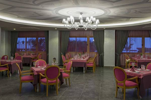 Innenbereich des Royal Taj Mahal Hotel Restaurants mit pinken Stühlen und Tischen, großen Fenstern und einer großen Kronleuchter.