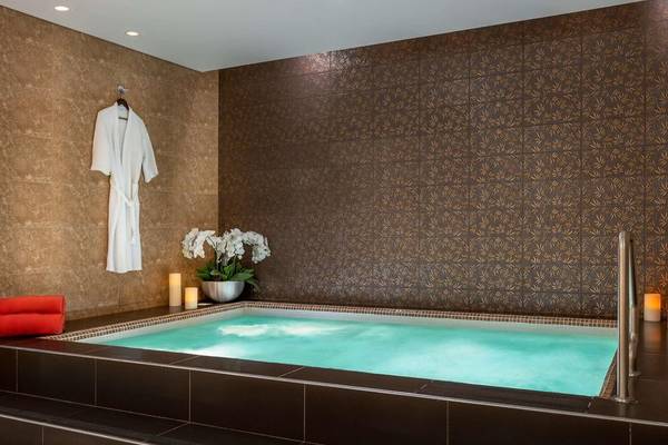 Jacuzzi im Badezimmer des Hyatt Regency Oryx Doha mit braunen Wänden, weißen Fliesen und Blumenvase.