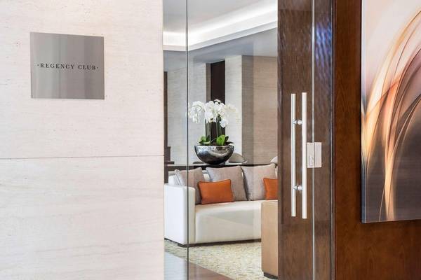 Eingang zum Regency Club im Hyatt Regency Oryx Doha mit weißer Couch, Kissen und Blumenvase.