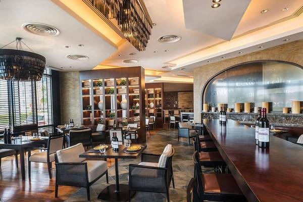 Innenansicht des Restaurants im Hyatt Regency Oryx Doha mit gedeckten Tischen, Stühlen und Flaschen auf der Theke.