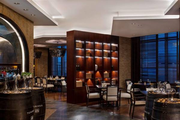 Innenansicht des Restaurants im Hyatt Regency Oryx Doha mit Holztischen, Stühlen und Weinflaschen.